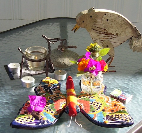 shows the altar, candles, ceramic butterfly, wooden chicken, mini bouquet of sunflower, bougainvillea and marigolds