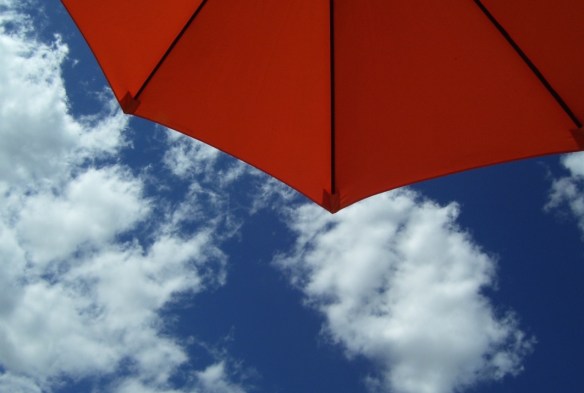 orange umbrella against blue sky with white puffy clouds